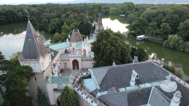 Blick vom Hohen Turm, © SLBG/Wolfgang Mastny Blick auf ein Schloss mit Türmen und einem See im Hintergrund, umgeben von Bäumen.