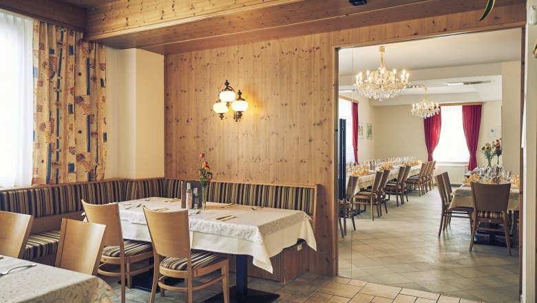 Ein gem&uuml;tliches Gastzimmer mit Holzw&auml;nden und ein angrenzender Festsaal mit Kronleuchtern und gedeckten Tischen.