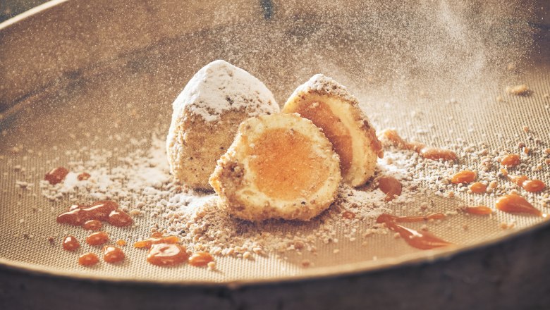 Eismarillenkn&ouml;del mit Puderzucker und Aprikosensauce auf einem Sieb.